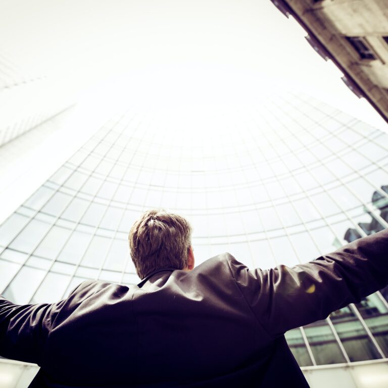 professional man standing in front of skyscraper with wide hands open showing sign of victory